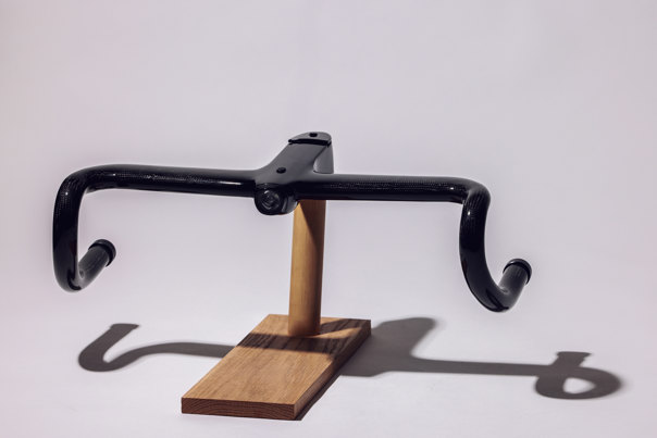 Black carbon-fibre bicycle handlebars mounted on a wooden display stand. 