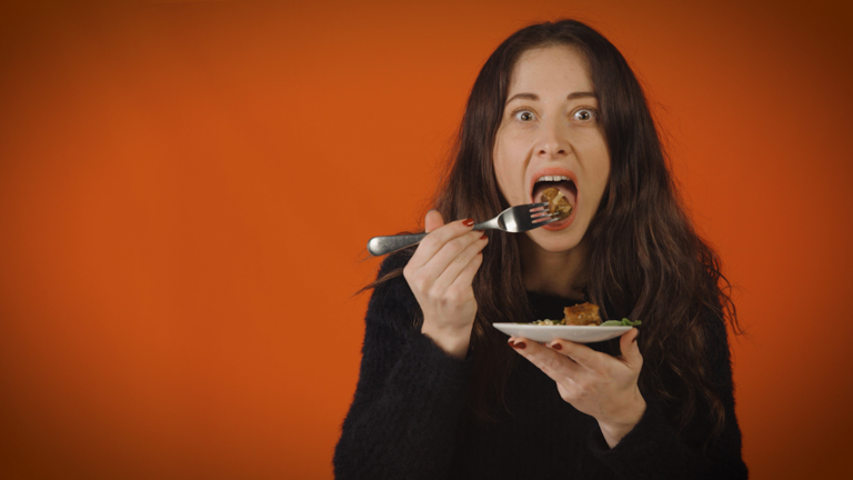 An apprehensive young woman is about to eat a mouthful of food.