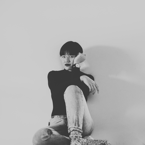 Black and white image of a woman sitting on the floor leaning a wall