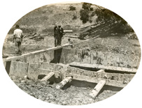 Three men standing on a beam across the coffer dam of Pier 3 of the permanent bridge over Woady Yallock Creek on the Gheringhap to Maroona line, 1912
