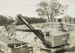 Construction of line, Yarrawonga, circa 1927-33. A Harman caterpillar-mounted steam shovel is loading ballast into rail trucks.