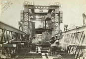Staff constructing the bridge over the Murray River, on the Strathmerton to Tocumwal line, Tocumwal, 1906. Workers are hot-riveting strengthening plates along the top chord of the span truss using portable forges and pneumatic riveting guns.