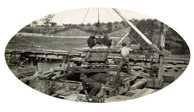 Two men manoeuvring a grab above the old bridge over the Mitchell River on the Bairnsdale to Orbost line, circa 1916