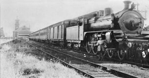 Staff member beside A2 class steam locomotive no. 985 hauling passenger carriages, circa 1930