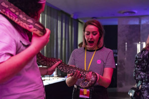 A woman with a look of exclamation on face as she meets a python being handle by a museum staff member