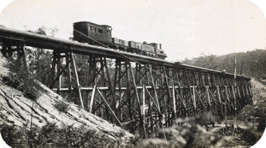 An R class steam locomotive and tender drawing two trucks and a guard's van over the completed Stony Creek Bridge, on the Bairnsdale to Orbost line, circa 1915