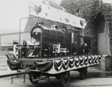 Railway-themed military recruitment display, Victoria, circa 1930. A model train stands on a flatbed truck. The train, which is decorated, carries a sign reading "Model of consolidation locomotive, the most powerful in the Commonwealth. Why not let it draw you to the front?"