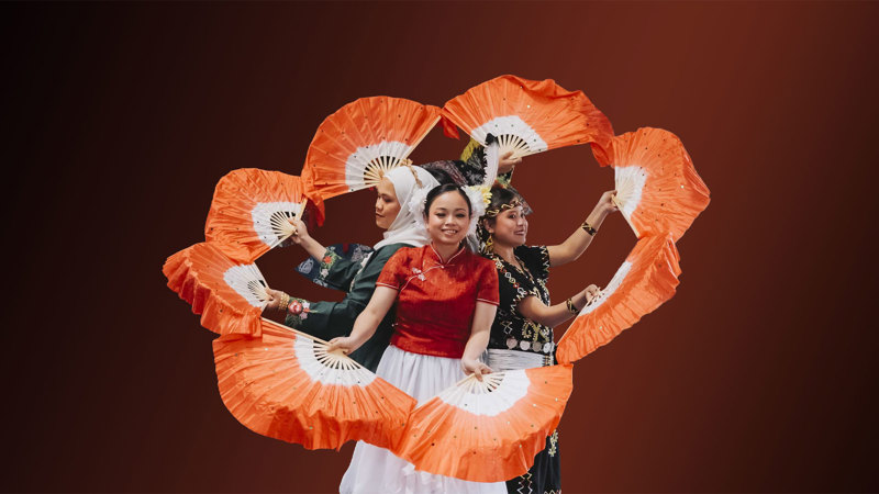 Four Malaysian dancers are performing a traditional dance standing a circle back-to-back and holding red-and-white fans.