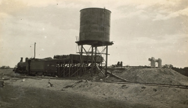 A steam locomotive beside a coal and tank stage at Balranald, circa 1927. There are railway tracks at a higher level behind the 24,000 gallon (109.2kl) water tank. Balranald was the last station of the Moama to Balranald line.