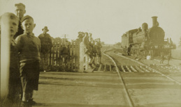 Steam locomotive no. D2 766 with passenger carriages attached at a crossing, circa 1925