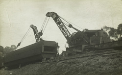 Two large cranes attempting to right an overturned railway carriage by means of cables around the carriage, circa 1910