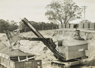 Construction of the Yarrawonga to Oaklands line, Yarrawonga, circa 1930. A Harman caterpillar-mounted steam shovel is loading ballast into rail trucks.