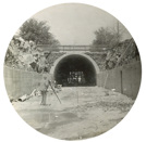 Tunnel construction on the South Kensington to West Footscray line, Footscray, 1928. A man with a theodolite stands in front of a tunnel.