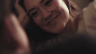 Still of a close up of a girl's face, smiling and looking at second figure