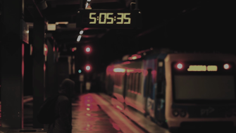 Still of digital clock on railway platform with train departing