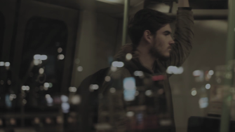 Still of a boy standing in a train with city lights reflected in window