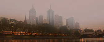 Wide shot of Melbourne city from the Southbank side, across the river, covered in smog, with a bridge in the background