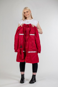 A girl with blonde hair holds a red jacket in front of her while smiling