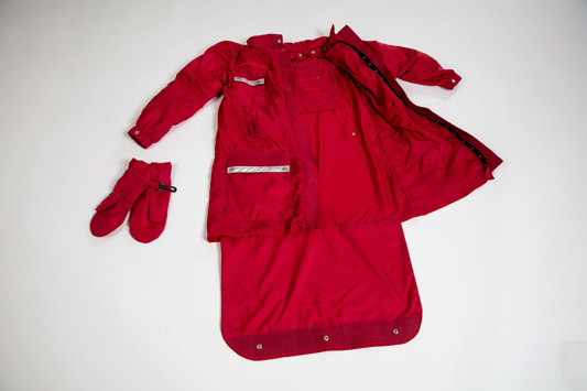 A red jacket is laid out flat on the ground and is opened up to display various components, such as gloves and storage compartments.