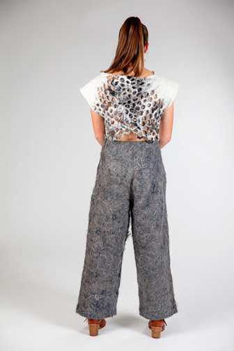 A girl is seen from standing from behind. She is wearing grey felted pants and a white felted top that has tesselleted detailing at the back. 