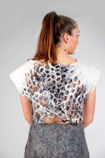 A white felted top, seen from the back. The back has a grey marbelled tessellated detail. The top is held together with felted pegs. 