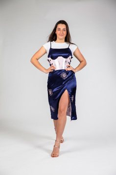 The model is walking towards the camera wearing a blue satin dress, worn over a white t-shirt. A pink resin brace is work over the dress.