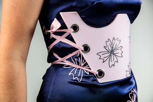 A close up of a pink resin brace that is secured using pink ribbon over a blue satin dress with pink floral detailing.