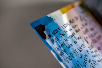 Close up of photograph of a colourful zine page with a sheet of transparent acetate adhered. The acetate has black hand-written text on it