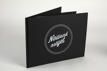 A copy of a black photobook stood up, titled 'Now and Not Yet'