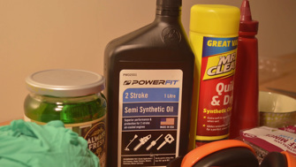 A selection of everyday items such as a bottle of car oil, Mr Clean, earmuffs are assembled alongside a jar of pickles and tomato sauce. 