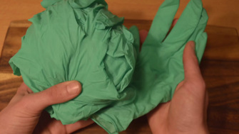 Hands holding green rubber gloves that are bunched to replicate the head and leaves of an iceberg lettuce. 