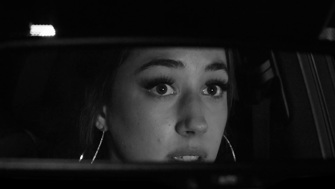 A close up of a girl wearing hoop earrings in the rear view mirror of a car.  She is looking at something in the mirror and looks frightened.