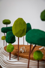 Closeup of green trees in 3D diorama with miniature swing set in background