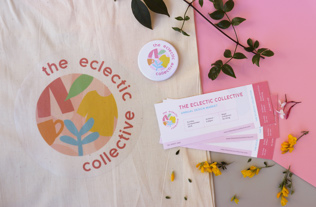 Photograph of branded tickets, tote bag and badge for 'The Eclectic Collective'. The branding is a circular logo consisting of colourful shapes and flower petals are scattered around the objects
