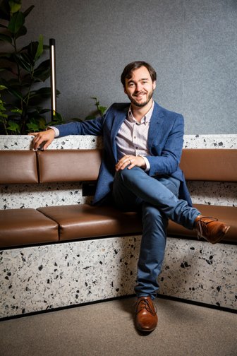 A portrait of a man in a blue suit sitting in a corner chair with brown shoes on