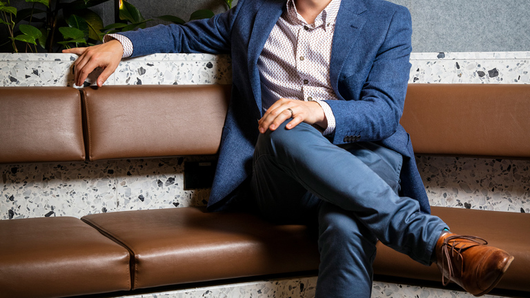 A portrait of a man in a blue suit sitting in a corner chair with brown shoes on