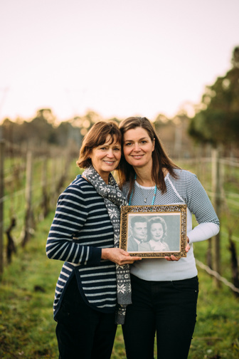 Two women in a vineyard holding a black and white photo. 