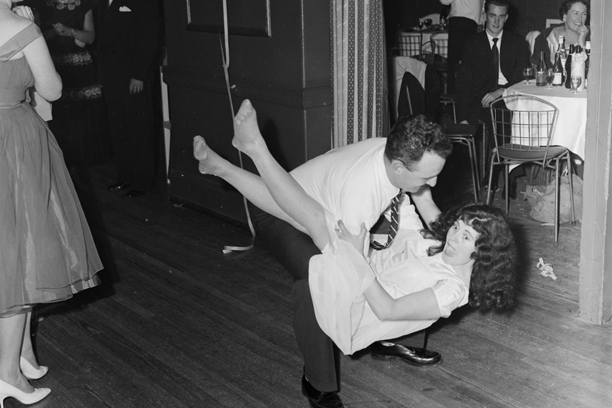 Couple dancing at a Swallow & Ariell social function held at 9 Darling Street reception center. The man is lifting the woman off the ground, behind them are people seated at tables.