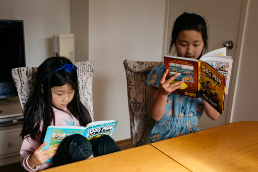 Two girls sitting at the dinner table reading