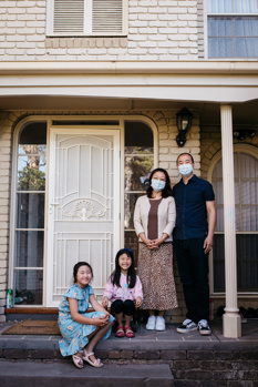 Family of four posing at the front door. The adults are wearing face masks