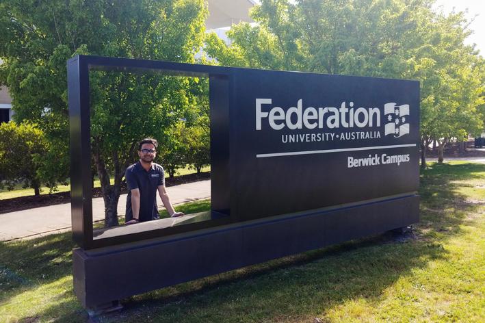 Man standing next to a university sign