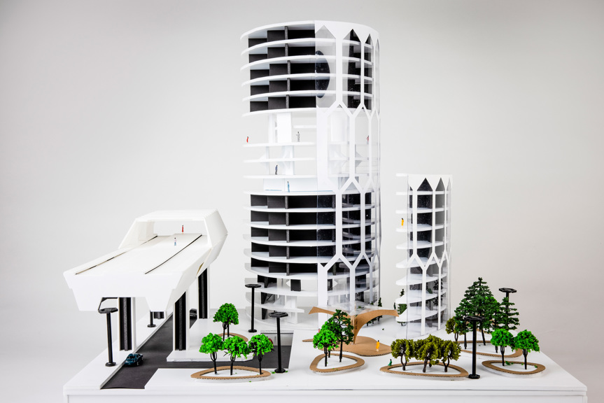 Architectural model of a high-rise building. The façade is cut in half to reveal the layout of floors. A train station is shown to the left of the building, with an entry to an underground car park located underneath.