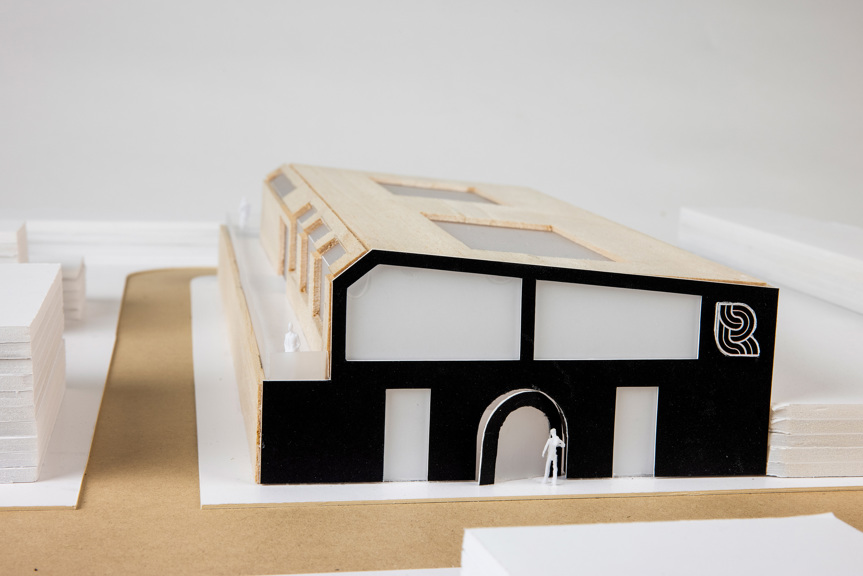 A close up of an architectural model with the Track Records logo. The building is two story’s high with a black front façade, a balcony along one side and two large windows in the roof.