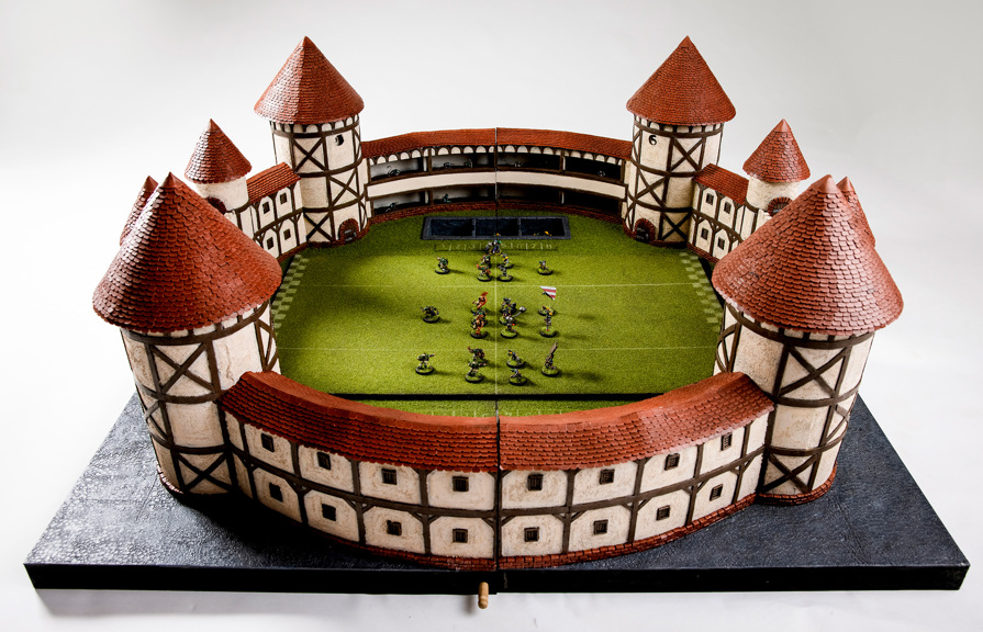 The ‘Blood Bowl’ Stadium is shown in full, with several miniature figures arranged on the stadium’s fake turf, as if a game was underway. The stadium is circular, with Tudor style walls and turrets.