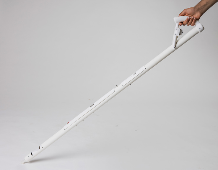 An image of a white cane made from plastic tubing. It is being held up by a hand. The cane has a switch in the middle and a sensor towards the base.