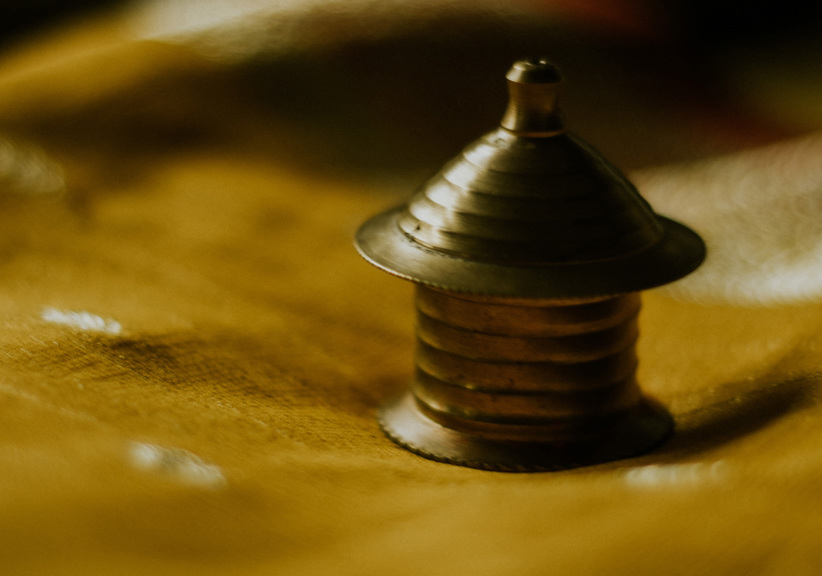 A close-up photograph of a golden item of jewellery, lying on a yellow saree. 
