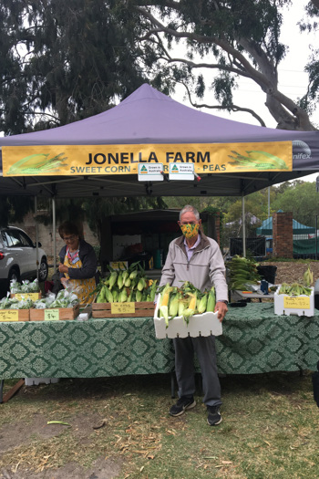 Man wearing a mask holding a box of corn in front of a market stall