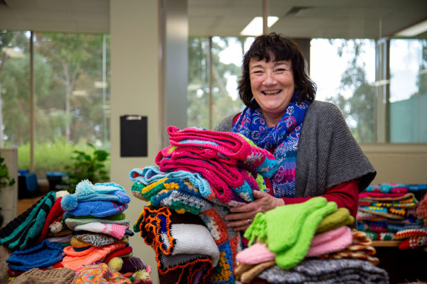 Woman standing with piles of knitting. She is smiling