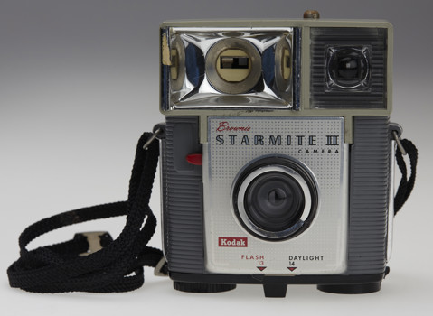 Small box camera with a flash. It has a black strap attached. The front of the camera is grey and silver