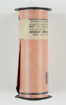 Black metal spool with cellulose nitrate film, sealed and covered in a protective pink paper cover and sealed with a printed Kodak sticker.